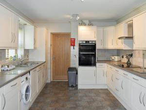 a large white kitchen with white cabinets and appliances at Ty Fynnon Cottage-Uk2786 in Penmaen-mawr +7 photos