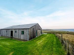 a wooden barn with a green field next to the ocean at Clarsach in Big Sand