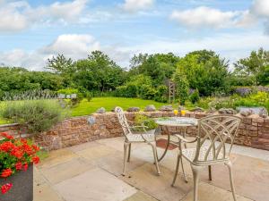 a patio with a table and chairs and a stone wall at The Stables in Cheddar