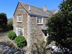 an old stone house with white windows and bushes at Barn Cottage in Saint Mawgan