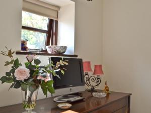 a desk with a computer monitor and a vase of flowers at Paper Mill Cottage in Sutton