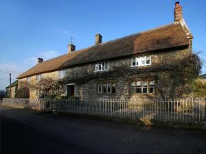 an old stone house with a fence in front of it at Grapevine Cottage in Stocklinch