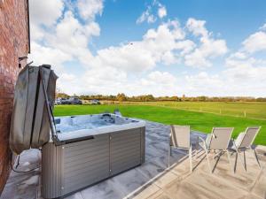 a hot tub on a patio with chairs and a field at Buckley Farm, Barn 1 - Uk36588 in Oswestry