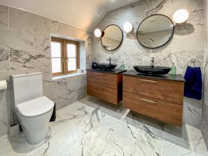 a bathroom with two sinks and a toilet and mirrors at Quabbs Head Cottage in Mathon