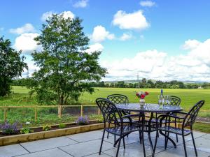 a table and chairs on a patio with a view of a field at Kingfisher Cottage in Kirkton of Airlie