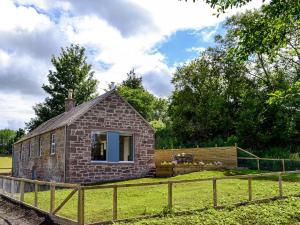 a small brick house in a field with a fence at Kingfisher Cottage in Kirkton of Airlie