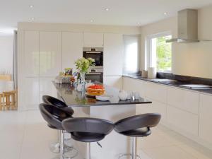a kitchen with white cabinets and a island with black chairs at Honey Pippin in Cheriton Bishop +22 photos
