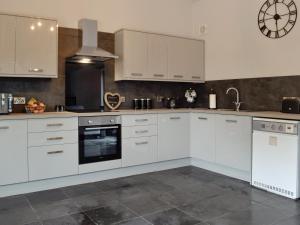 a kitchen with white cabinets and a clock on the wall at Caffi Sali - Weluk143 in Blaenpenal