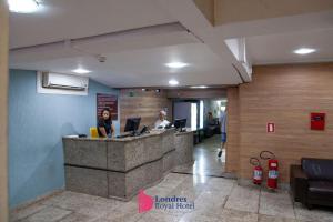 a lobby with two people sitting at a reception desk at Londres Royal Hotel in Londrina