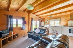a living room with a leather couch and a kitchen at Moor View Cabin (Oak Tree Lane) in Okehampton
