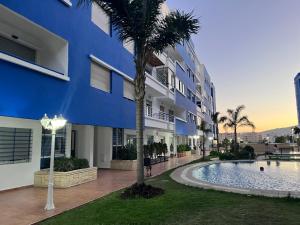 a blue building with a palm tree next to a swimming pool at Spacious Family Apartment - Air Conditioning, Pool & Garden Views in Martil