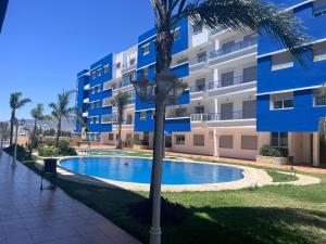 a palm tree next to a building with a swimming pool at Spacious Family Apartment - Air Conditioning, Pool & Garden Views in Martil