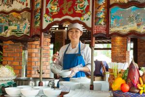 a woman is holding a bowl in front of a table at Pandanus Resort in Mui Ne