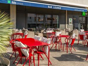 a group of red tables and chairs in front of a restaurant at IBIS STYLES ALES CENTRE in Alès