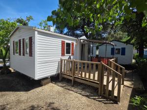 a small white tiny house with a wooden porch at Vias Plage - Camping Les Salisses - Mobilhome in Vias
