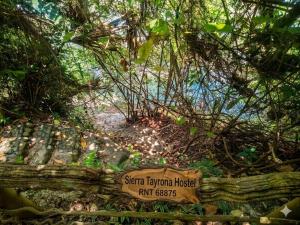 a sign in a forest with a beach in the background at Sierra Tayrona hostel in El Zaino