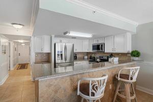 a kitchen with white cabinets and a counter with two bar stools at Islander E 7011 Stunning oceanfront condo with pool & gym access in Fort Walton Beach