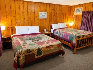 two beds in a room with wooden walls at Cedars Motel in Saint Ignace