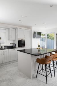 a white kitchen with a black counter and chairs at Castlecroft House with Hot Tub in Dungiven