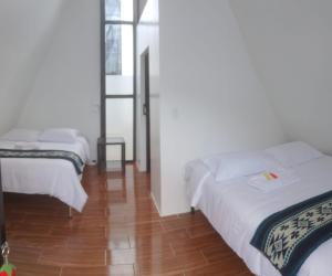 a bedroom with two beds and a wooden floor at Tungurahua Eco Lodge INN BAÑOS in Quillullaco
