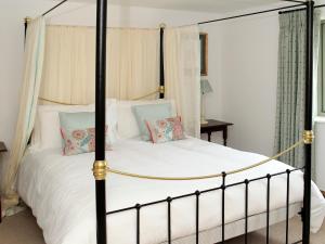 a bedroom with a canopy bed with white sheets and pillows at Kites Gate Cottage in Kingham