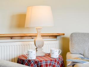 a table with a lamp and two mugs on it at Osprey Cottage - Uzq in Kirkton of Airlie