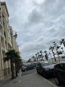 a street with cars parked on the side of a street with palm trees at Cozy Beach Apartment Diar Mansour Rabat in Rabat