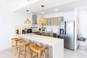 a kitchen with a counter with stools and a refrigerator at The Friendly Condo by AcoModo Punta Caelo in El Nance