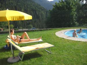 two women sitting on lounge chairs under an umbrella next to a pool at Residence Wiesenheim in Trodena