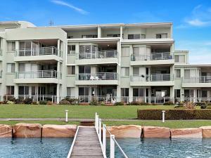 a large apartment building with a dock in front of it at Toukley Waterfront Apartment with Balcony - Outdoor Pool - Secure Parking - Wi-Fi - By HappyHosts in Toukley