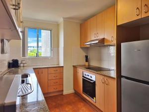 a kitchen with wooden cabinets and a white refrigerator at Toukley Waterfront Apartment with Balcony - Outdoor Pool - Secure Parking - Wi-Fi - By HappyHosts in Toukley