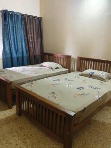 two twin beds in a room with blue curtains at Devaki Tourist Home in Ambalapulai +1 photo