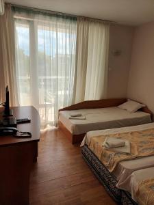 a bedroom with two beds and a desk and a window at Къща за Гости ,,Afrikana,, in Sveti Vlas