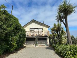 a house with a deck and a palm tree at Kakanui Surf Bach in Kakanui