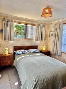 a bedroom with a large bed and two windows at Kakanui Surf Bach in Kakanui