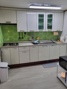 a kitchen with white cabinets and a green wall at 씨하우스 501호 in Hakch'ŏn-dong