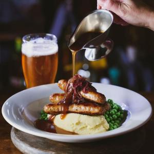 a plate of food with sausage and peas and a drink at The Pelican Inn in Stapleford