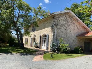 a large white building with a tree and a driveway at Maison en pierre cosy chez Laëtitia in Auros