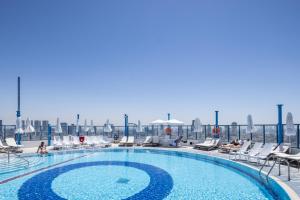 a swimming pool with chairs and people sitting around it at Superb Beachfront Apartments with Shelter by Sea N' Rent in Tel Aviv +200 photos