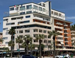 a tall white building with palm trees in front of it at Noa Apartments in Vlorë