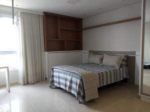 a bedroom with a bed with a striped blanket and a window at Dna Smart Style in Goiânia