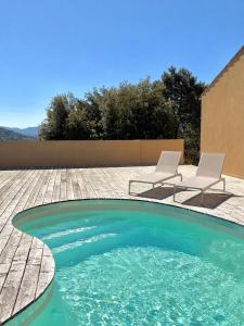 a swimming pool with two chairs and a table at Hôtel Aghjola in Pioggiola