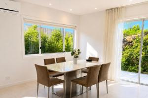 a dining room with a table and chairs and windows at 17 Pimpama Home in Pimpama