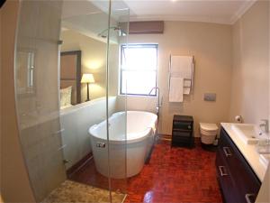 uma casa de banho com uma banheira e um chuveiro em vidro. em Rosebank Lodge Guesthouse by Claires em Joanesburgo