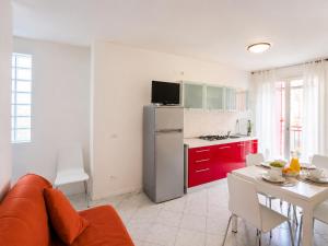 a living room with a couch and a kitchen with red cabinets at Residence Al Mare - Monolocale con Terrazza - Agenzia Cocal in Caorle