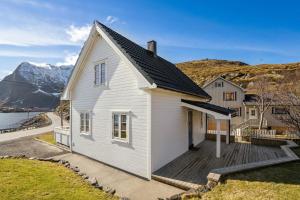 a white house with a deck next to the water at The Reine Scenic View in Moskenes