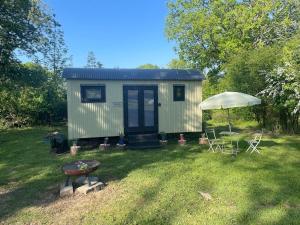 a tiny house in a yard with a table and an umbrella at Apple Orchard Shepherd Huts in Staple Cross