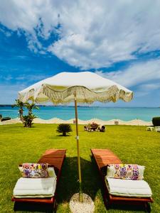 two beds under an umbrella in a field with the beach at Villa Incanto on the Sea in Syracuse