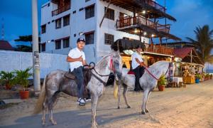 two men riding horses on a street in front of a building at Cocoa Beachfront Inn in Canoa