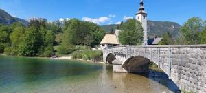a stone bridge over a river with a church at Apartma Rožmarin Bohinj in Bohinj